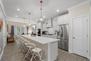 A modern kitchen with white cabinetry, stainless steel appliances, and a central island with bar stools.