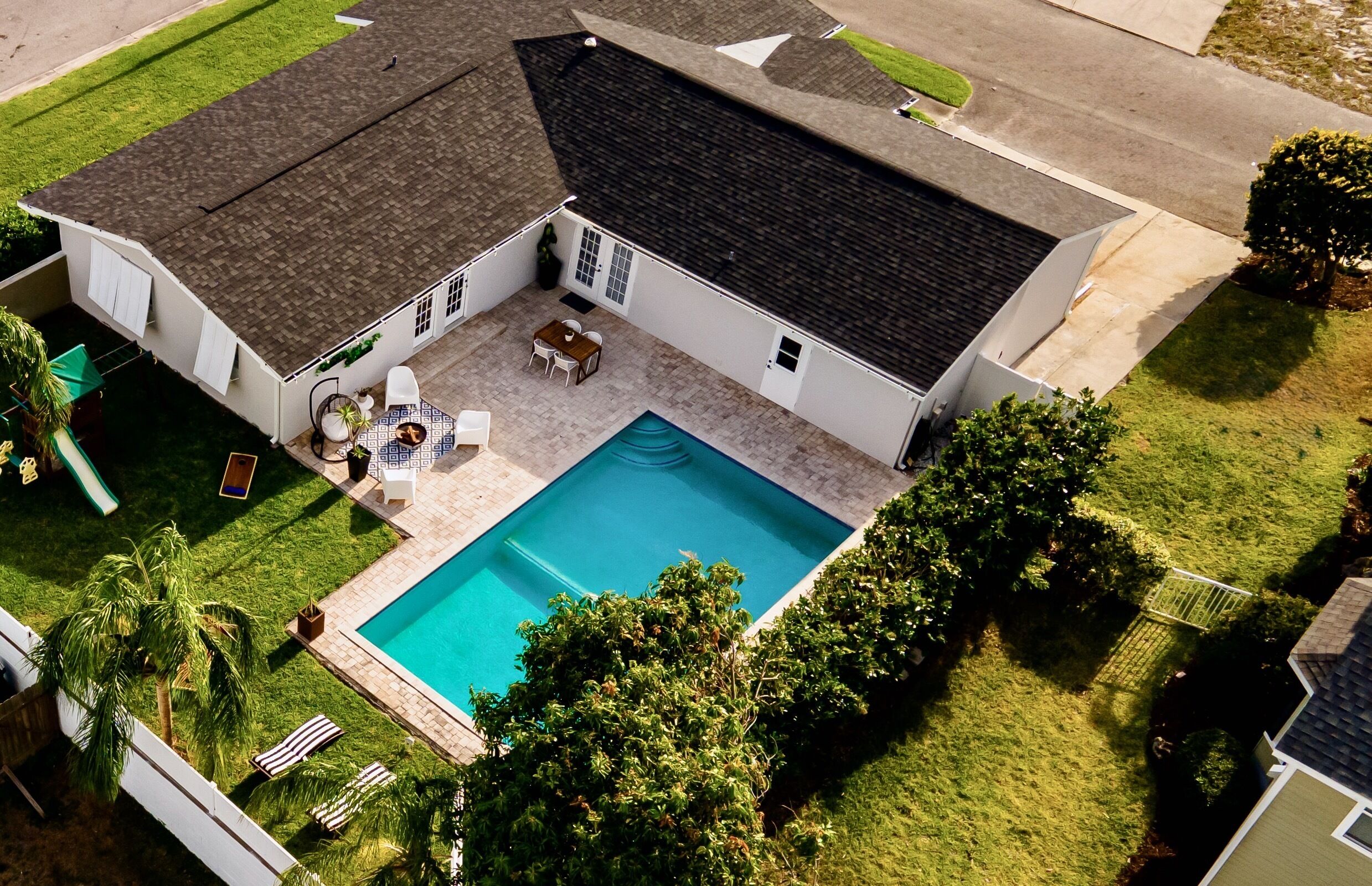 A house with a swimming pool, a patio with outdoor furniture, and a well-maintained lawn.