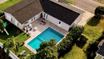 A house with a swimming pool, a patio with outdoor furniture, and a well-maintained lawn.