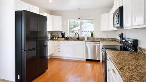 A modern kitchen with white cabinets, a black refrigerator, stainless steel dishwasher, and granite countertops. - 10 min to Beach, Peloton, Game Room, King Bed (Bradenton)