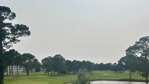 A view of a golf course with a pond, trees, and a building in the background. - Callaway Corner | Luxe Pet-Friendly 2BR Condo (Myrtle Beach)