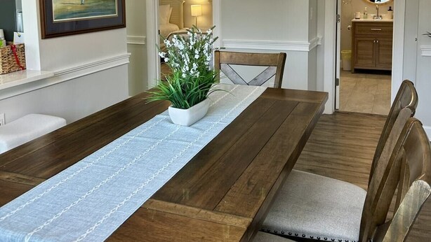 A dining room with a wooden table, chairs, a chandelier, and artwork on the walls. - Callaway Corner | Luxe Pet-Friendly 2BR Condo (Myrtle Beach)