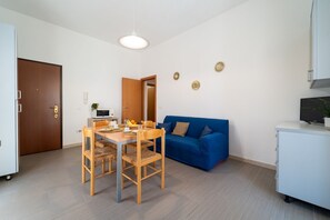 A compact living space with a dining table, chairs, a blue sofa, a kitchenette, and a television.