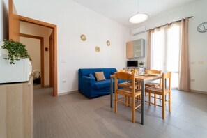 A modern living space with a dining area, a blue sofa, and a kitchen in the background.