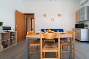A dining area with a table, chairs, and a blue sofa. There is a microwave and a cabinet in the background.