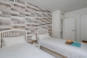 Een slaapkamer met twee bedden, een houten wandpaneel, een witte deur en een hoed op het bed.