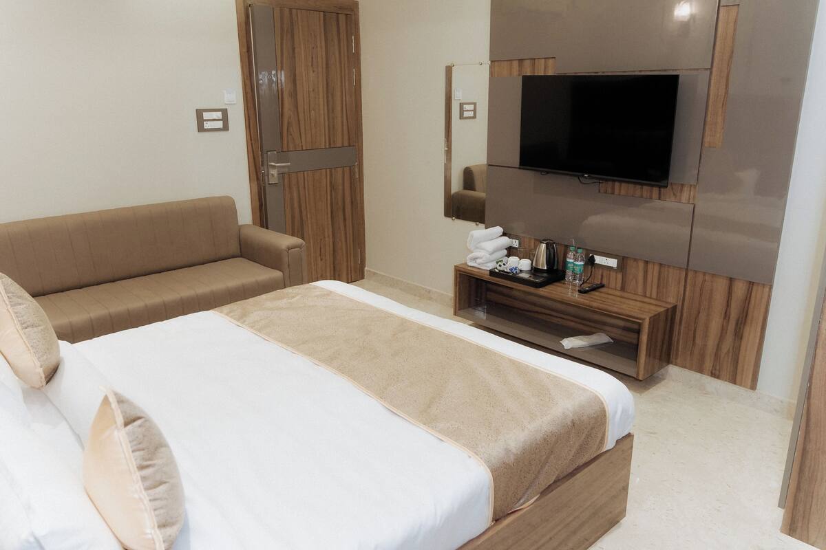 Une chambre d’hôtel avec un grand lit, un canapé, une télévision et une petite table en bois sur laquelle sont posés des articles de toilette.