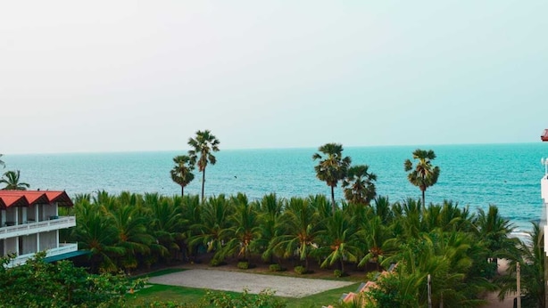 Un hotel frente al mar, con vistas al océano, rodeado de palmeras y un césped cuidado.