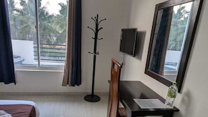 Habitación de hotel con cama, escritorio, silla, perchero, televisor y ventana con cortinas.