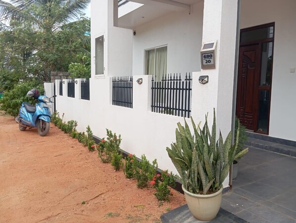 A white building with a black metal fence, a blue scooter parked outside, and a potted plant in the foreground. - Trinco Star Hotel (Trincomalee)