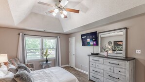Un dormitorio con cama, cómoda, televisor y ventilador de techo.