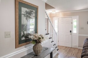 Staircase leads to an upper floor, with a framed photograph and a woven basket on the wall.