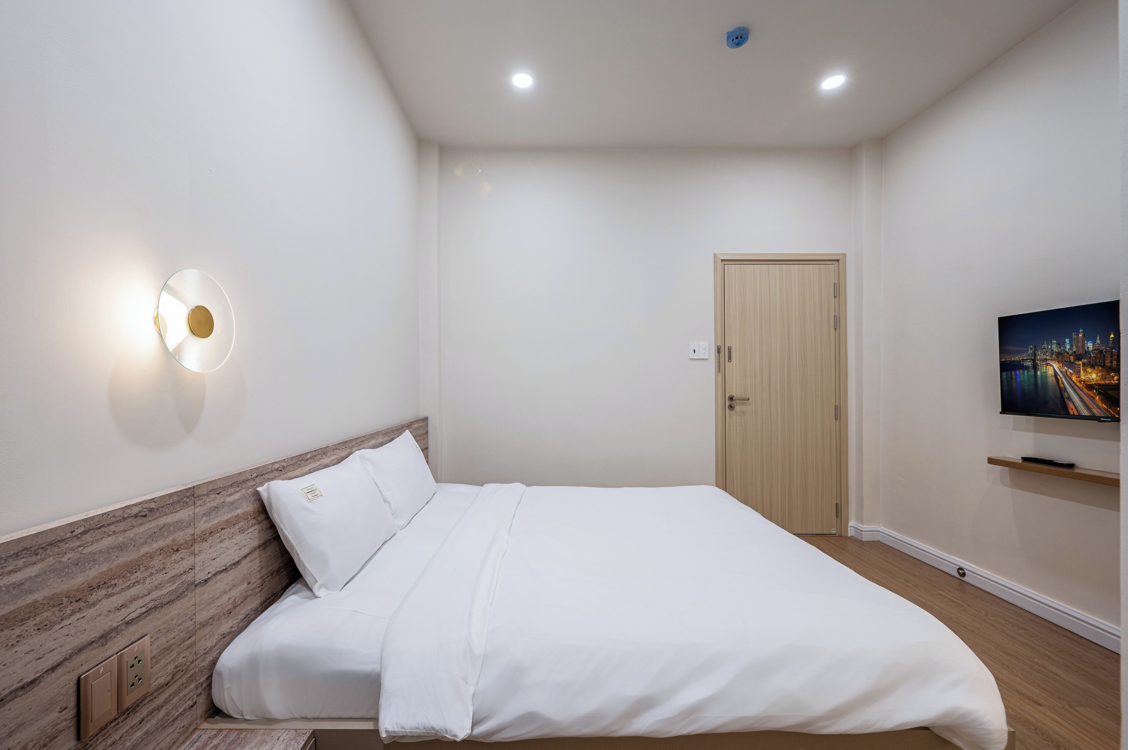 A neatly arranged hotel room with a bed, a wall-mounted TV, and a door.