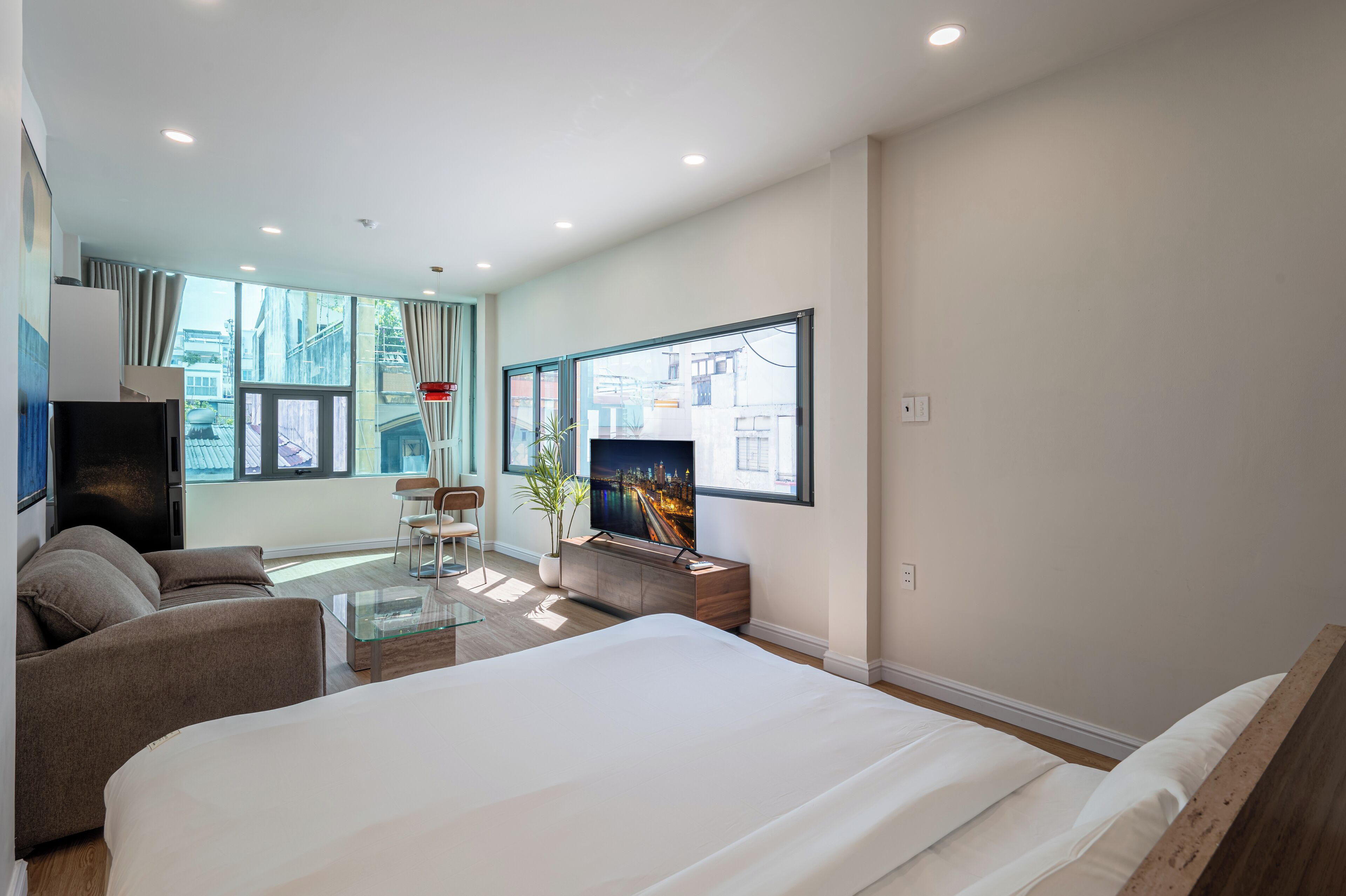 A modern hotel room with a large bed, a TV, a sofa, and a dining area.