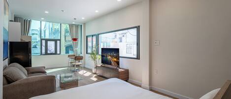 A modern hotel room with a large bed, a TV, a sofa, and a dining area.