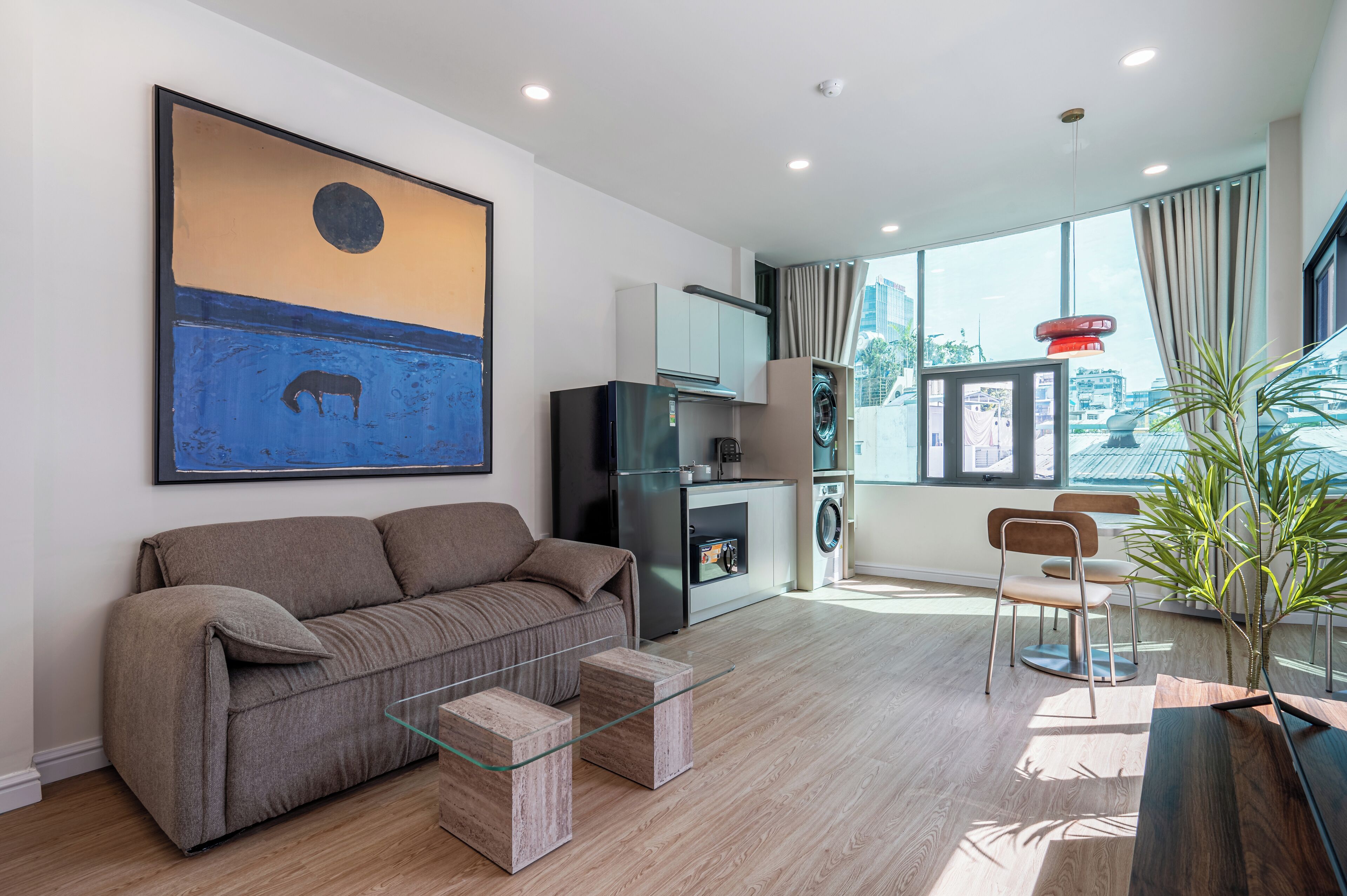 A modern living room with a sofa, a glass coffee table, a washing machine, and a dining area with a chair and table.