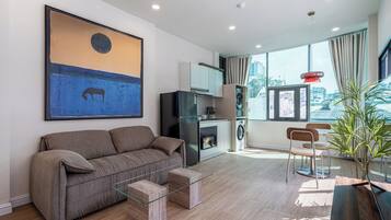 A modern living room with a sofa, a glass coffee table, a washing machine, and a dining area with a chair and table.