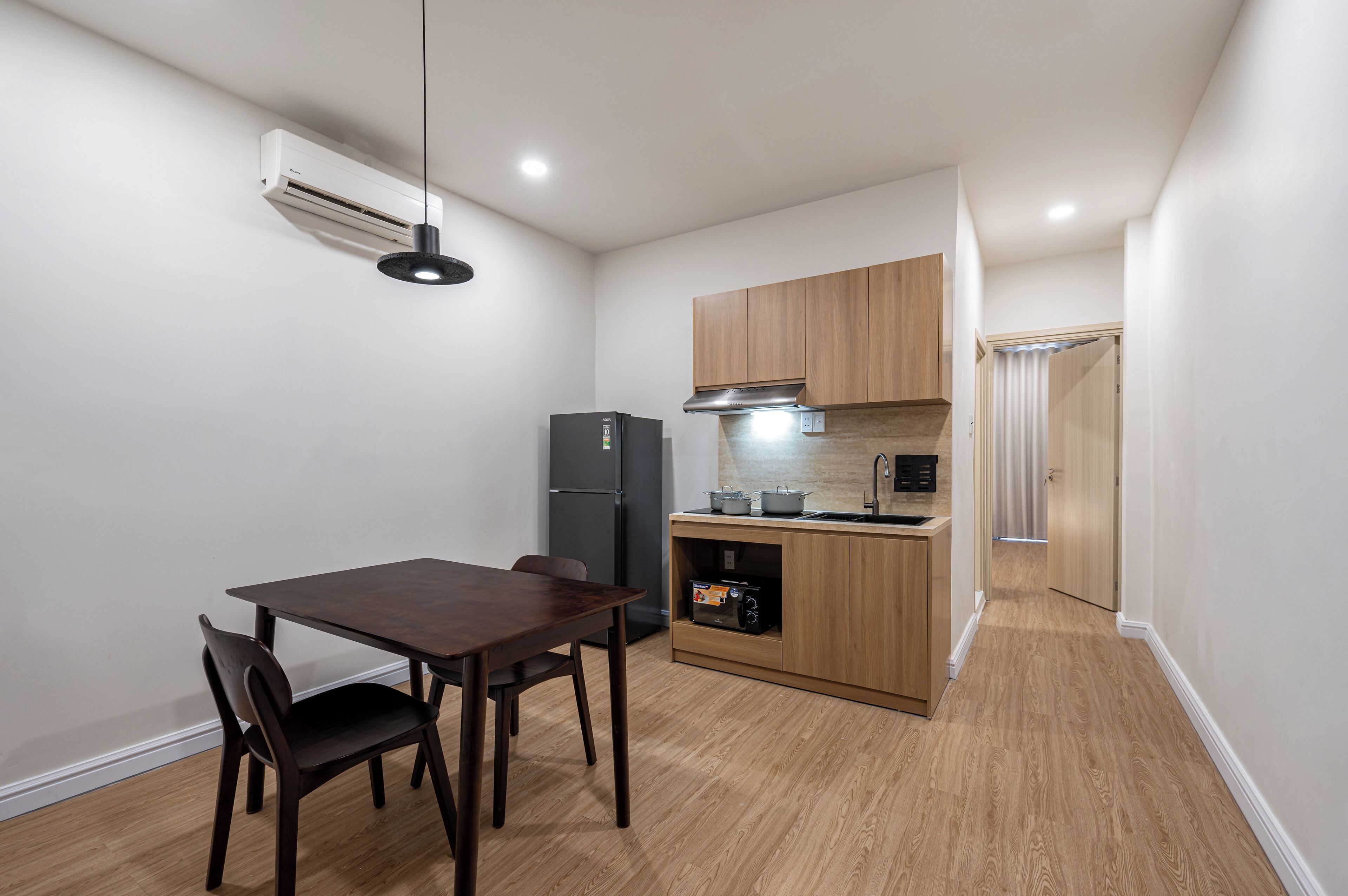 A compact kitchen with a dining table, chairs, a refrigerator, a microwave, and wooden cabinets.