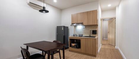 A compact kitchen with a dining table, chairs, a refrigerator, a microwave, and wooden cabinets.