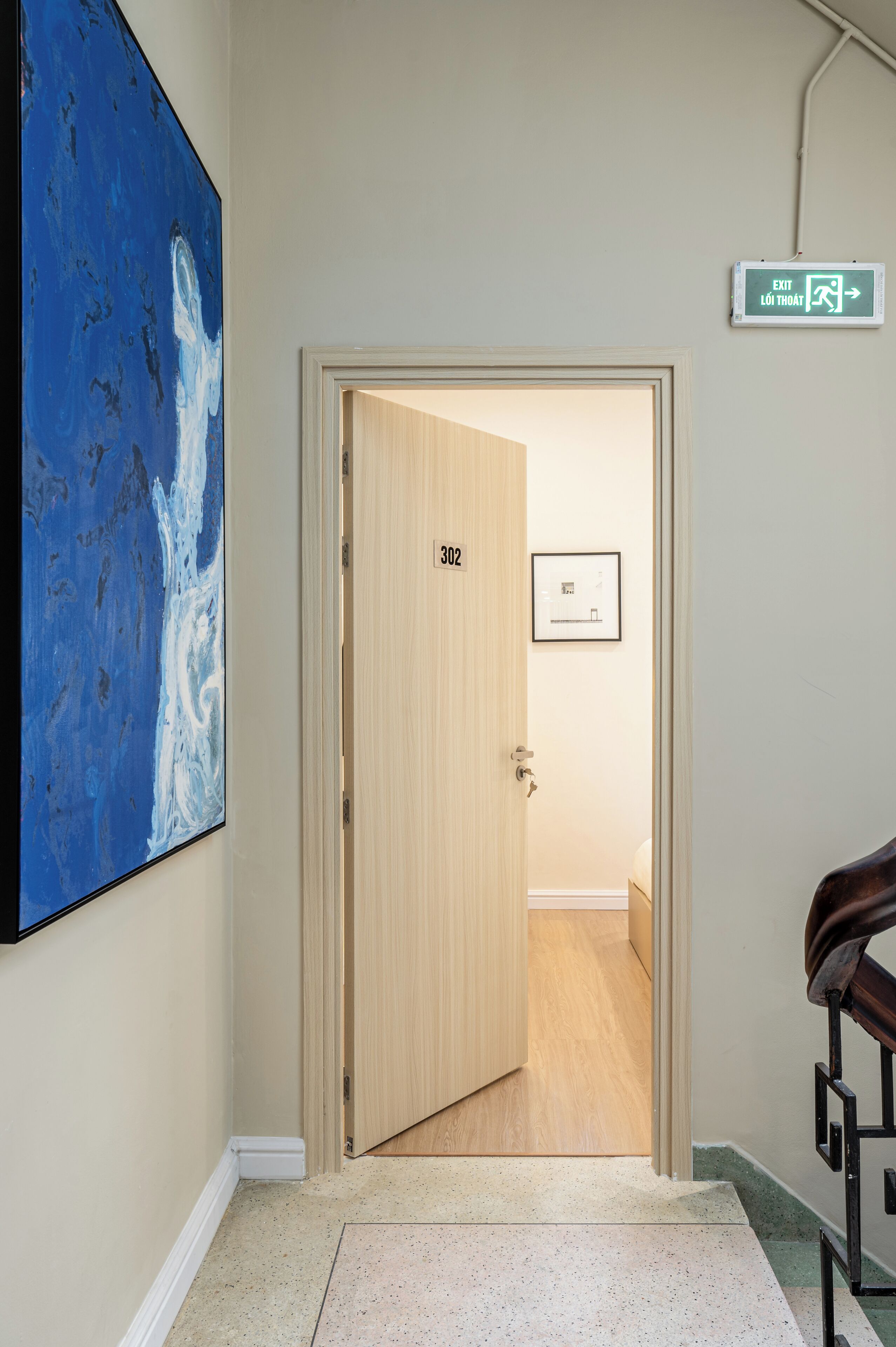 A hallway with a door labeled '302' leading to a room, a framed picture on the wall, and an exit sign.
