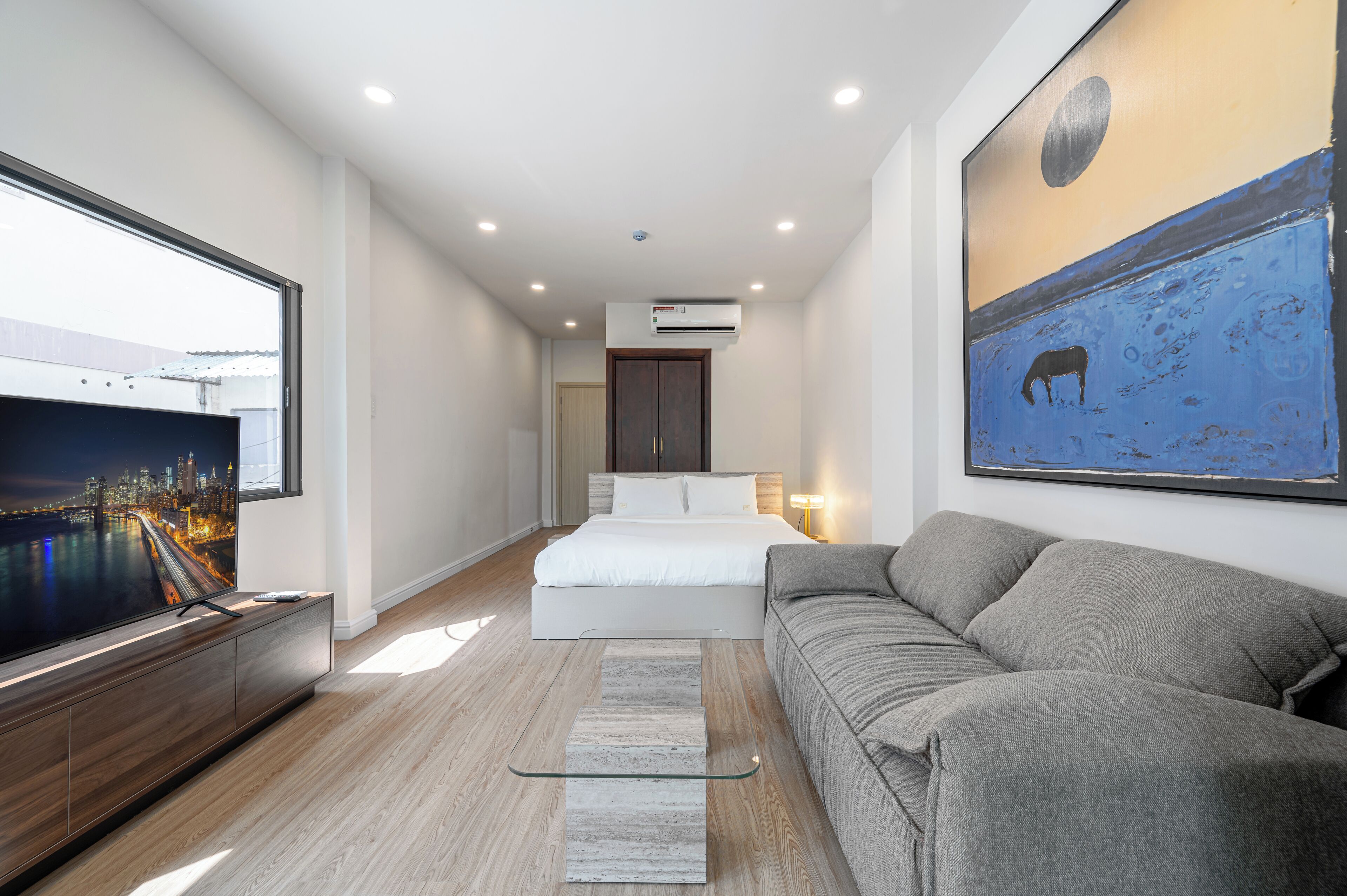 Una habitación de hotel moderna con un televisor grande, una cama, un sofá y un cuadro en la pared.