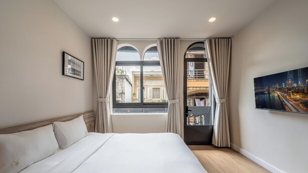 Une chambre d’hôtel avec un grand lit, une vue sur la ville par la fenêtre et un tableau au mur.