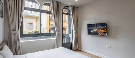 A hotel room with a bed, curtains, a TV, and a cityscape view.