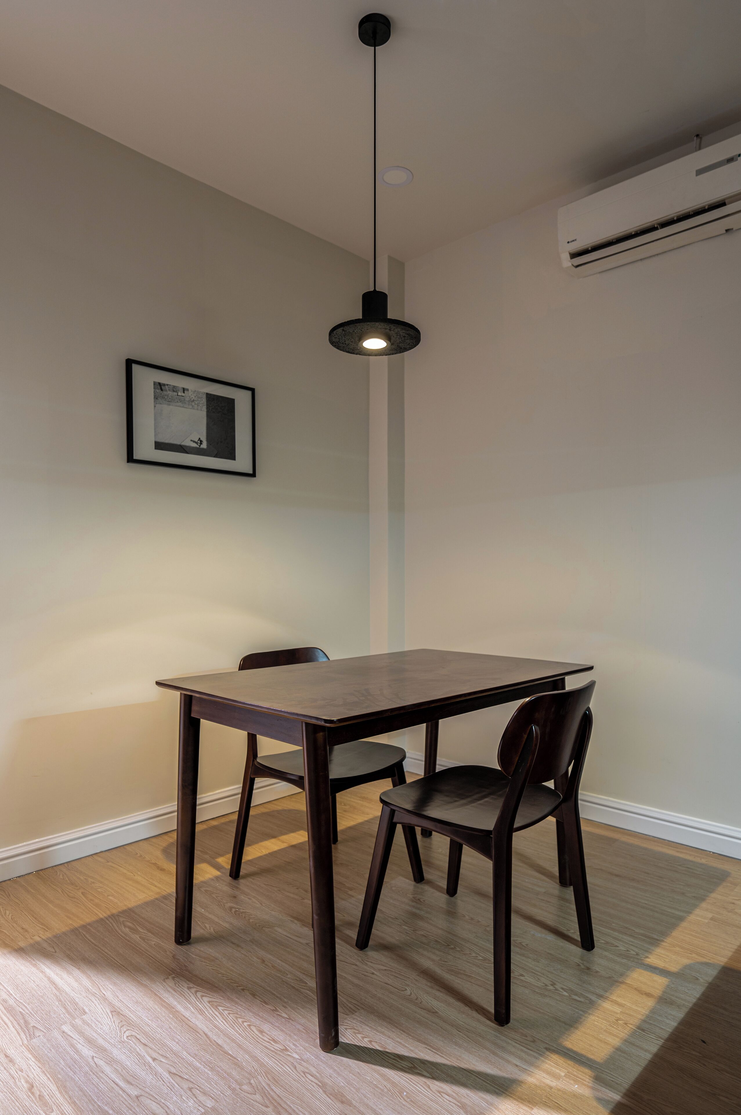 A dining area with a wooden table and chairs, a pendant light, and a framed picture on the wall.