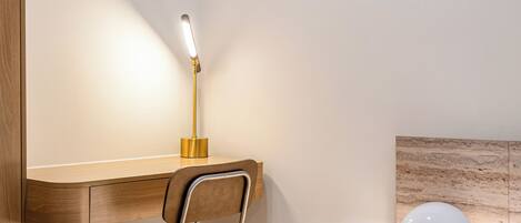 A modern bedroom with a wooden desk, a chair, a bedside lamp, and a bed.