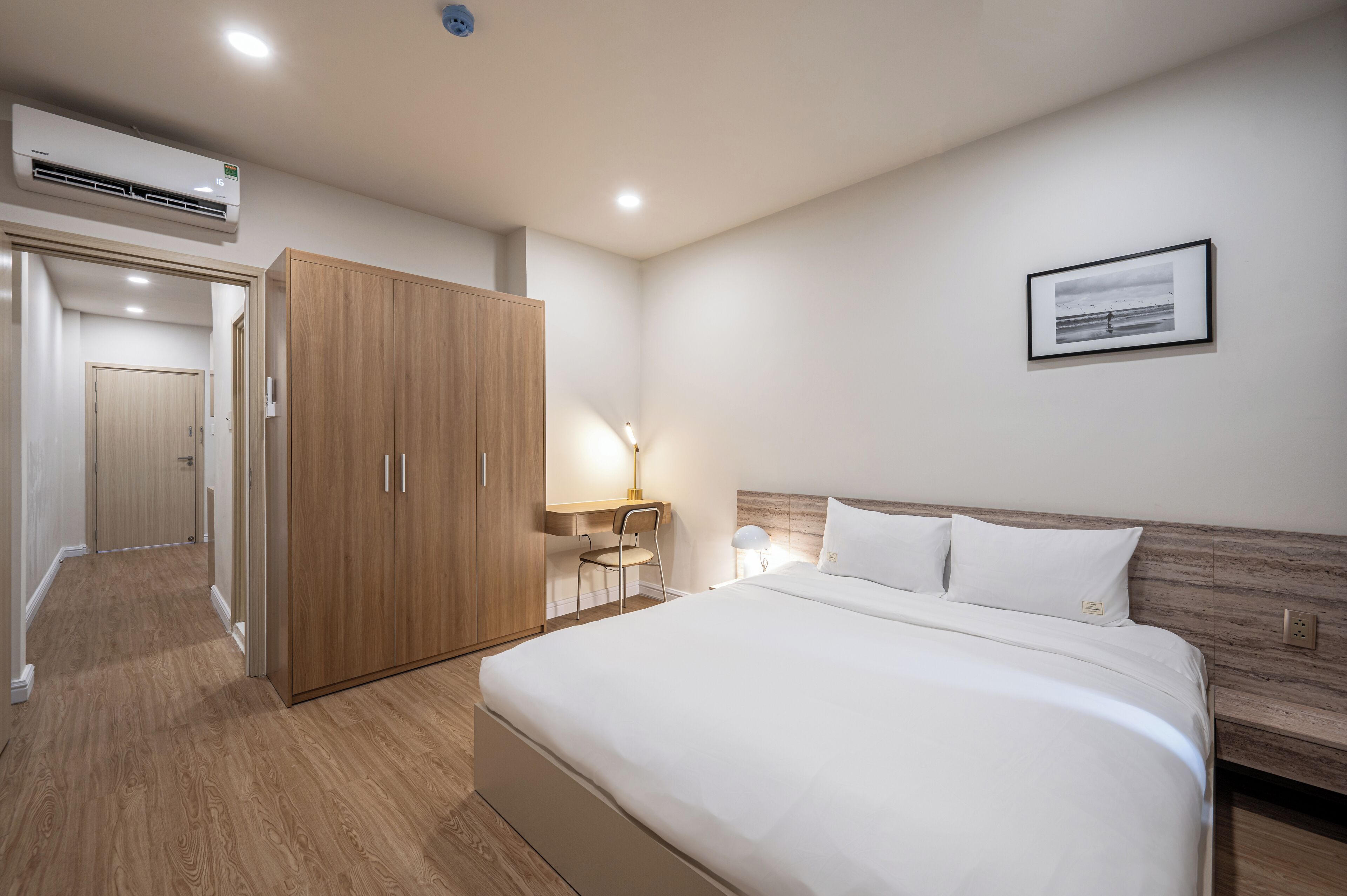 A hotel room with a large bed, wooden wardrobe, desk, chair, and a framed picture on the wall.