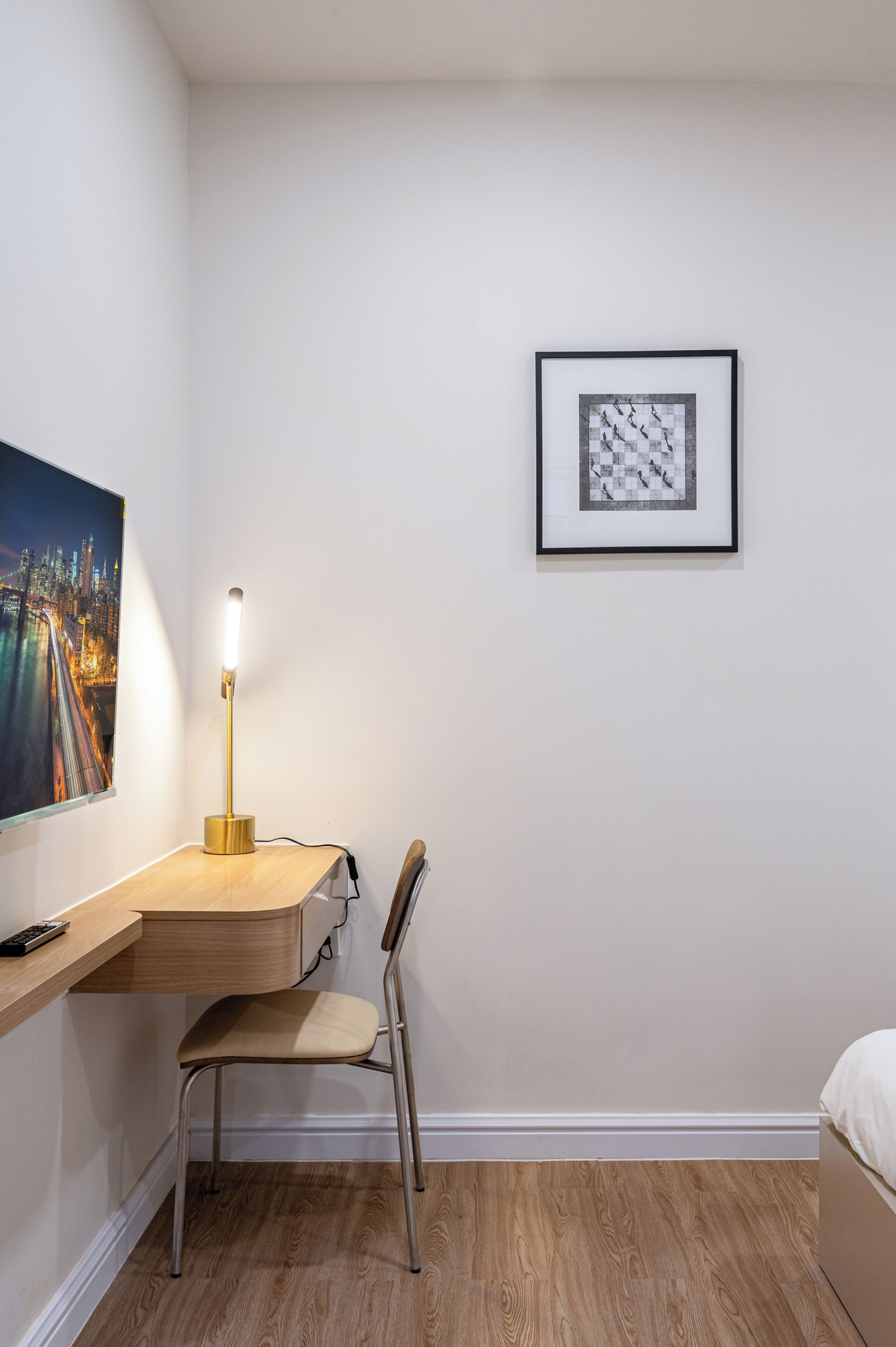 A modern room with a wooden desk, a chair, a framed picture on the wall, and a bed.