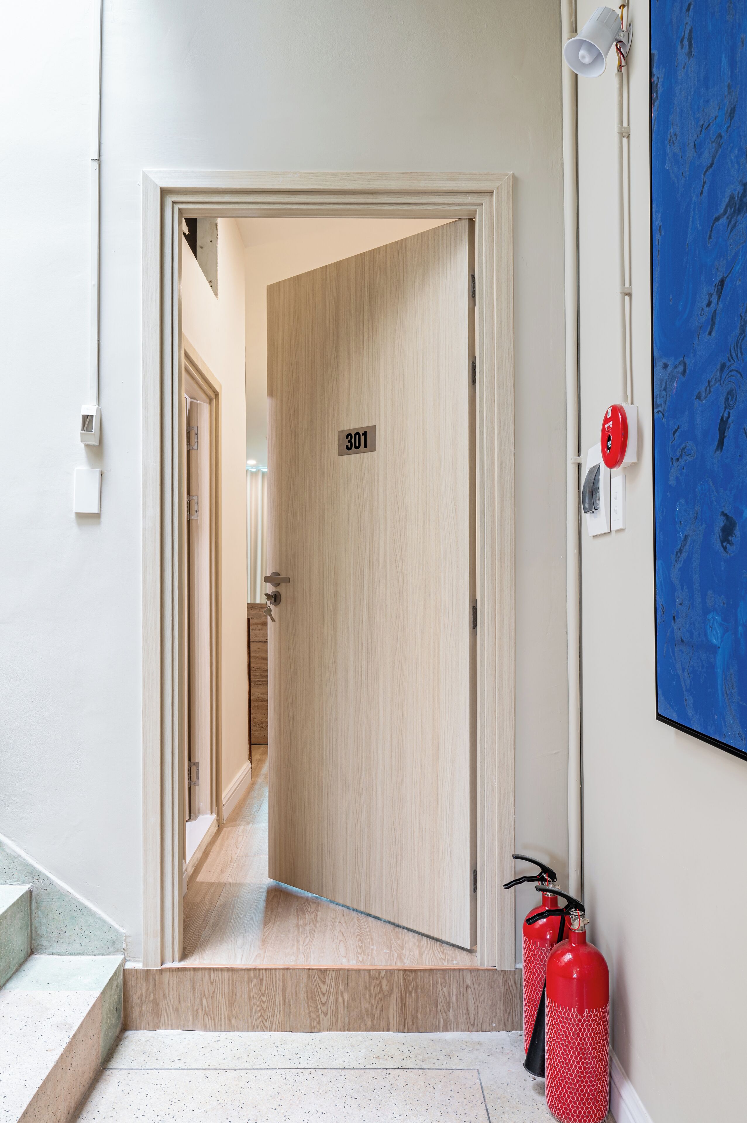 A hallway with a wooden door labeled "301", a fire extinguisher, and a wall-mounted light fixture.