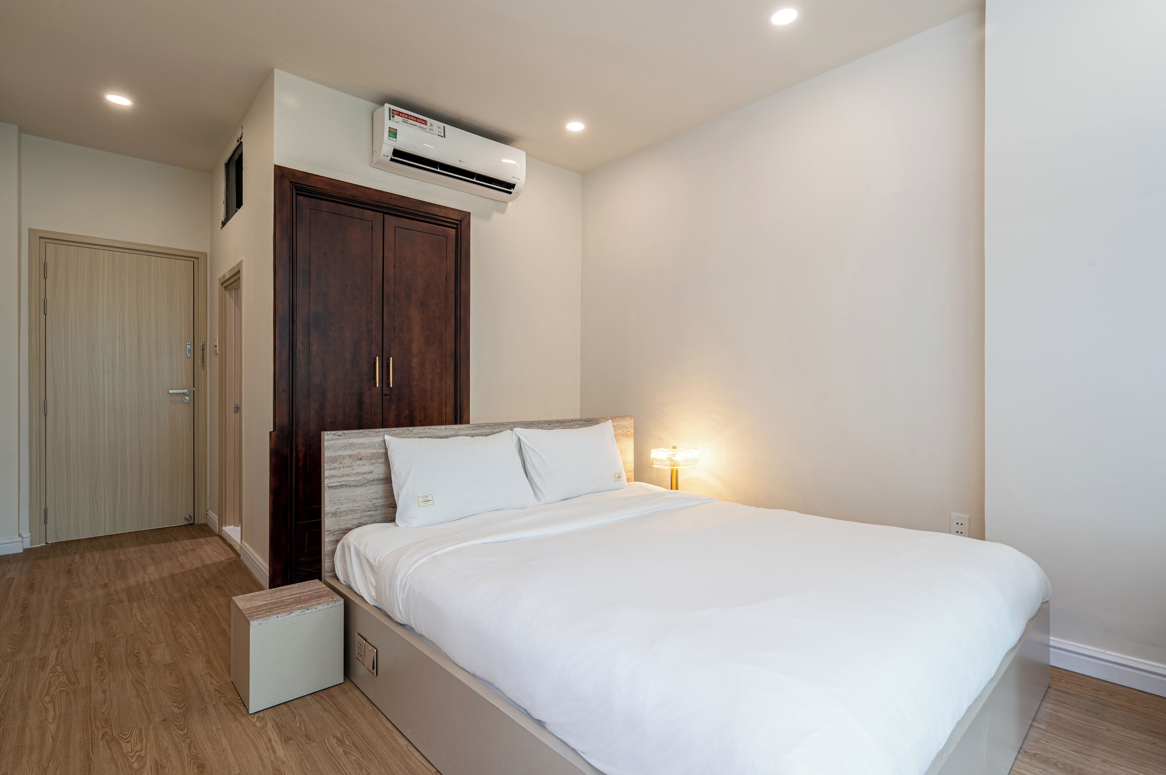 A bedroom with a bed, a wardrobe, an air conditioning unit, and a bedside lamp.