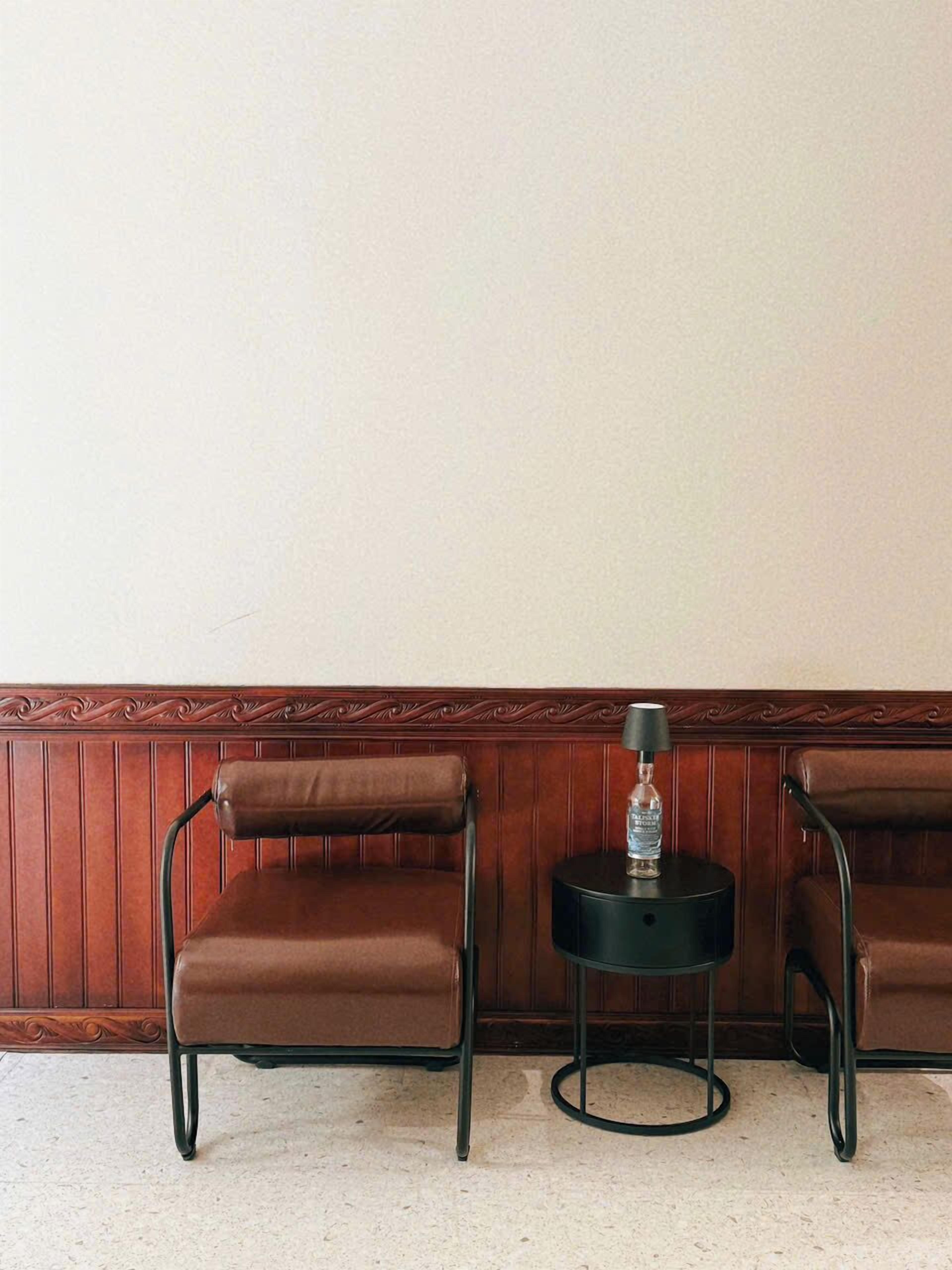 A corner of a room with two brown leather chairs and a small black table with a bottle on it.