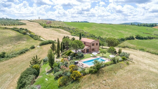 Una casa grande con piscina rodeada de exuberante vegetación y colinas.