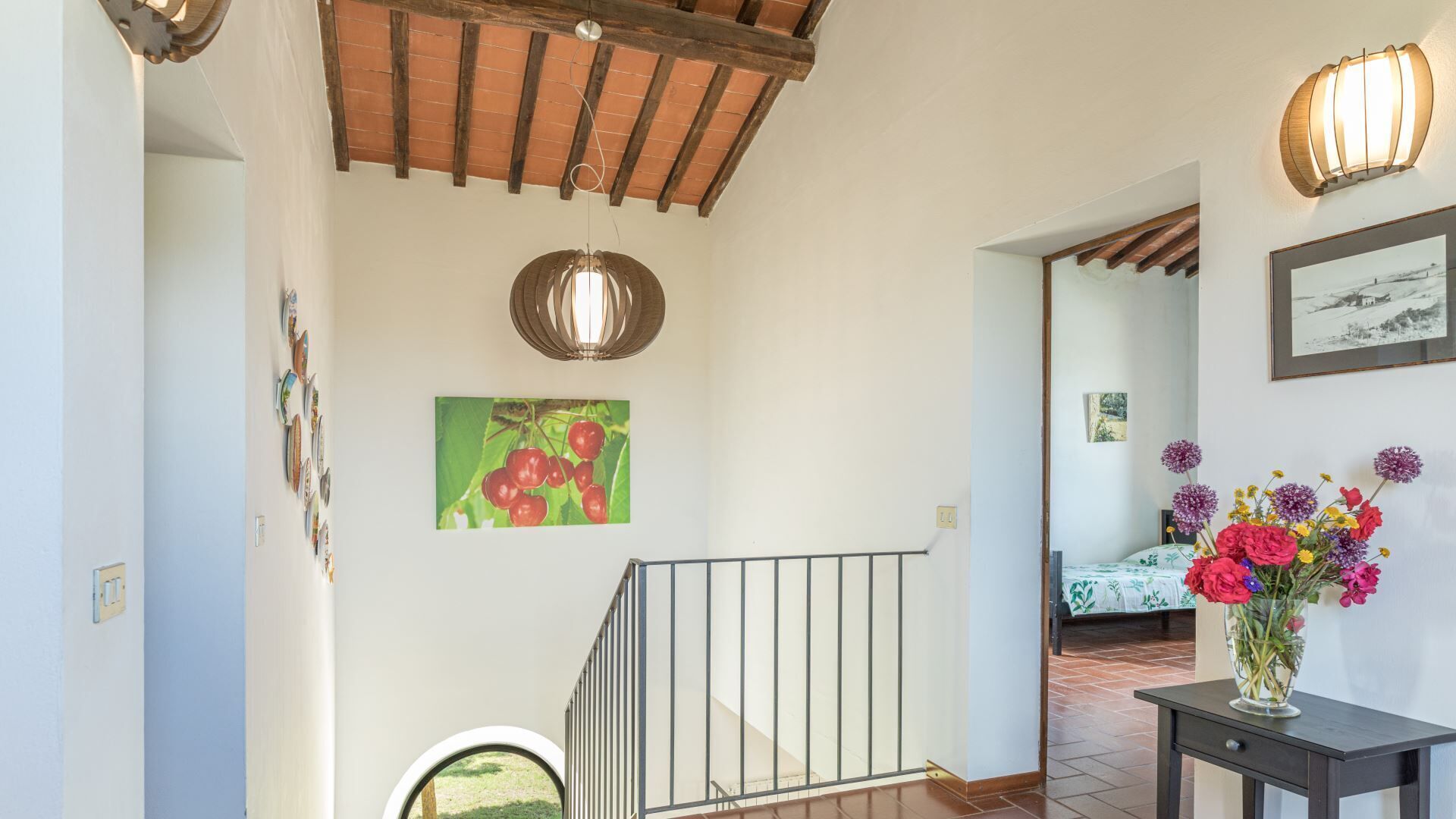 Un escalier avec une rampe en métal, un plafond en bois et un mur orné d’un tableau encadré et d’un vase de fleurs.