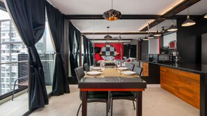 A modern dining area with a large table set for four, a kitchen with a black countertop, and a city view through large windows.