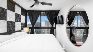 A modern hotel room with a large bed, a ceiling fan, a round mirror, and a city view.