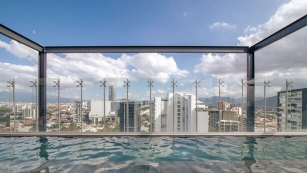 A rooftop infinity pool with a city view, surrounded by a glass enclosure.
