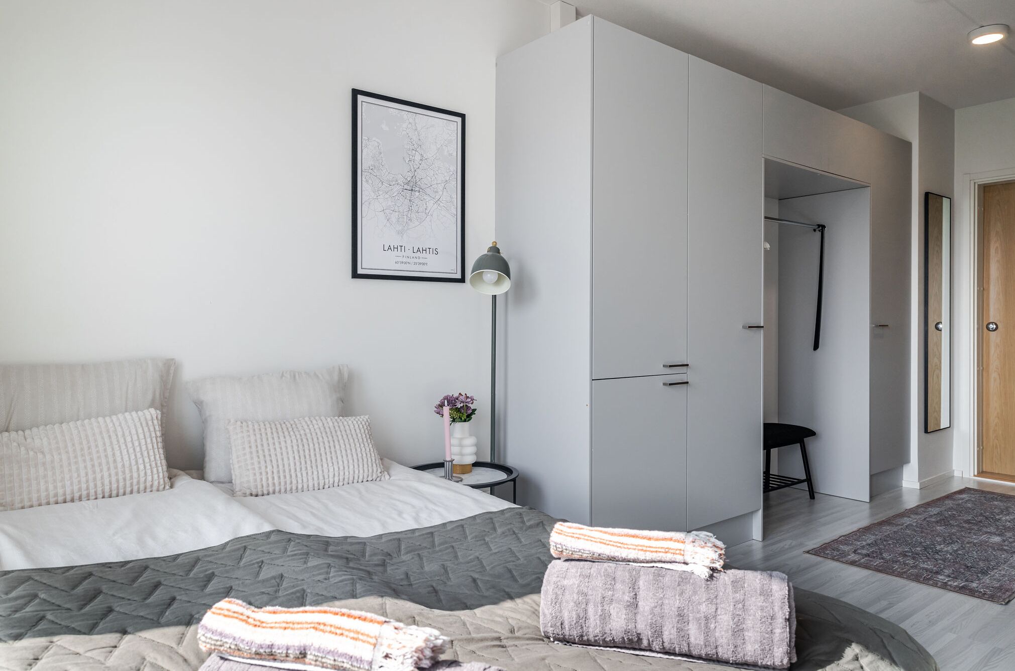 A modern bedroom with a bed, grey wardrobe, and a framed map on the wall.
