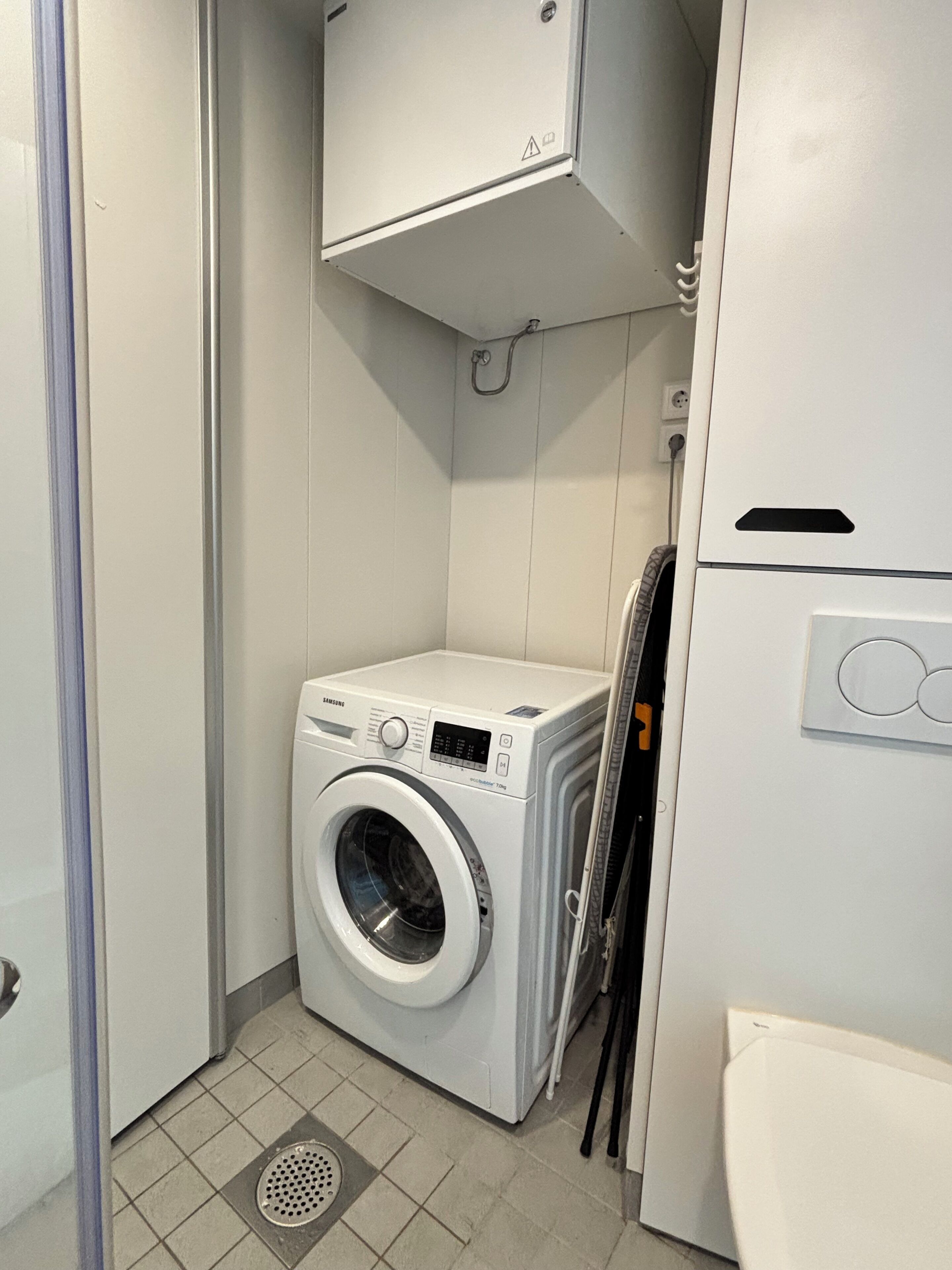 A compact laundry room with a front-loading washing machine, a dryer, and a small cabinet above the machine.