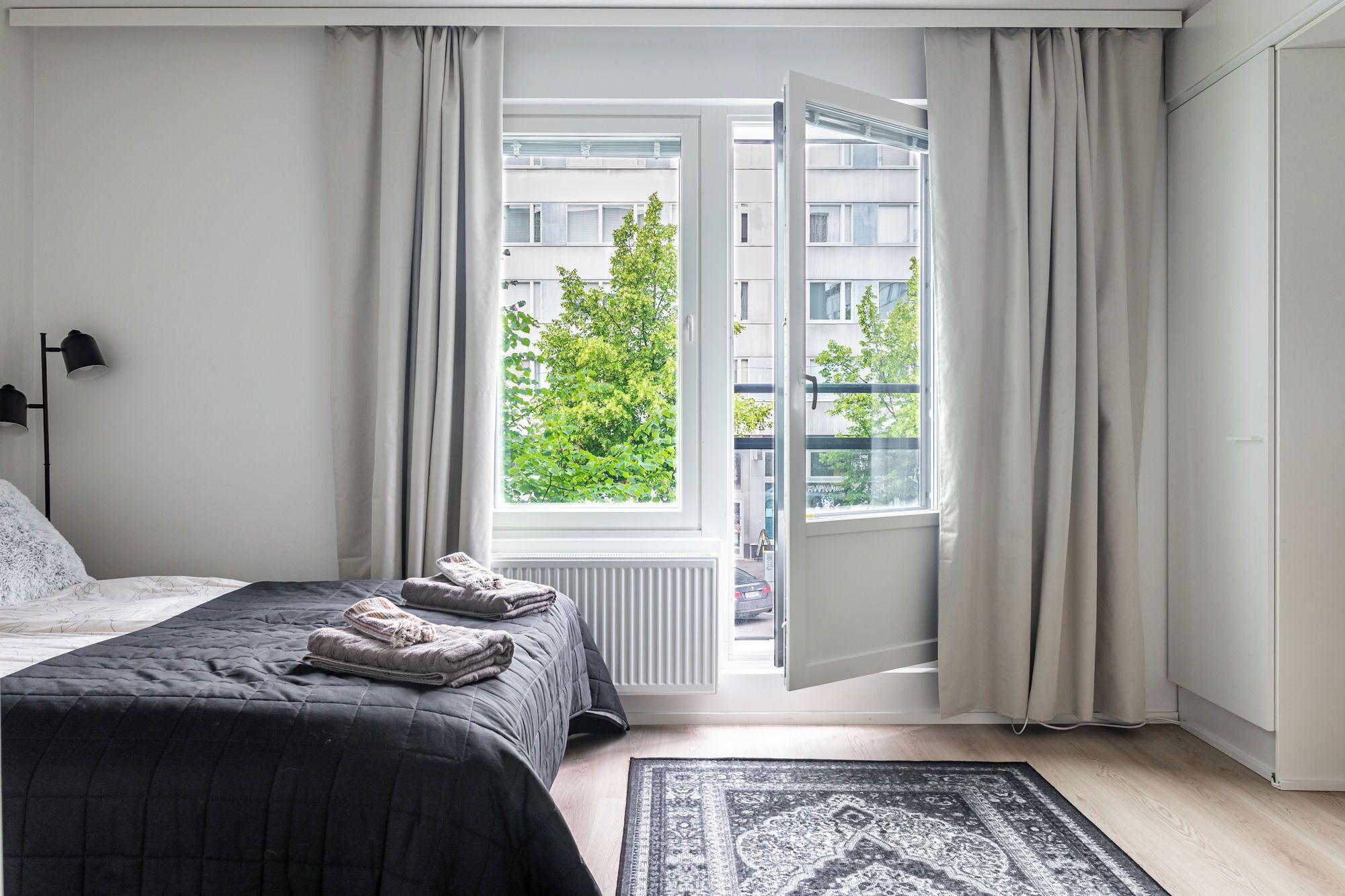 A bedroom with a bed, a window with curtains, a radiator, and a rug.