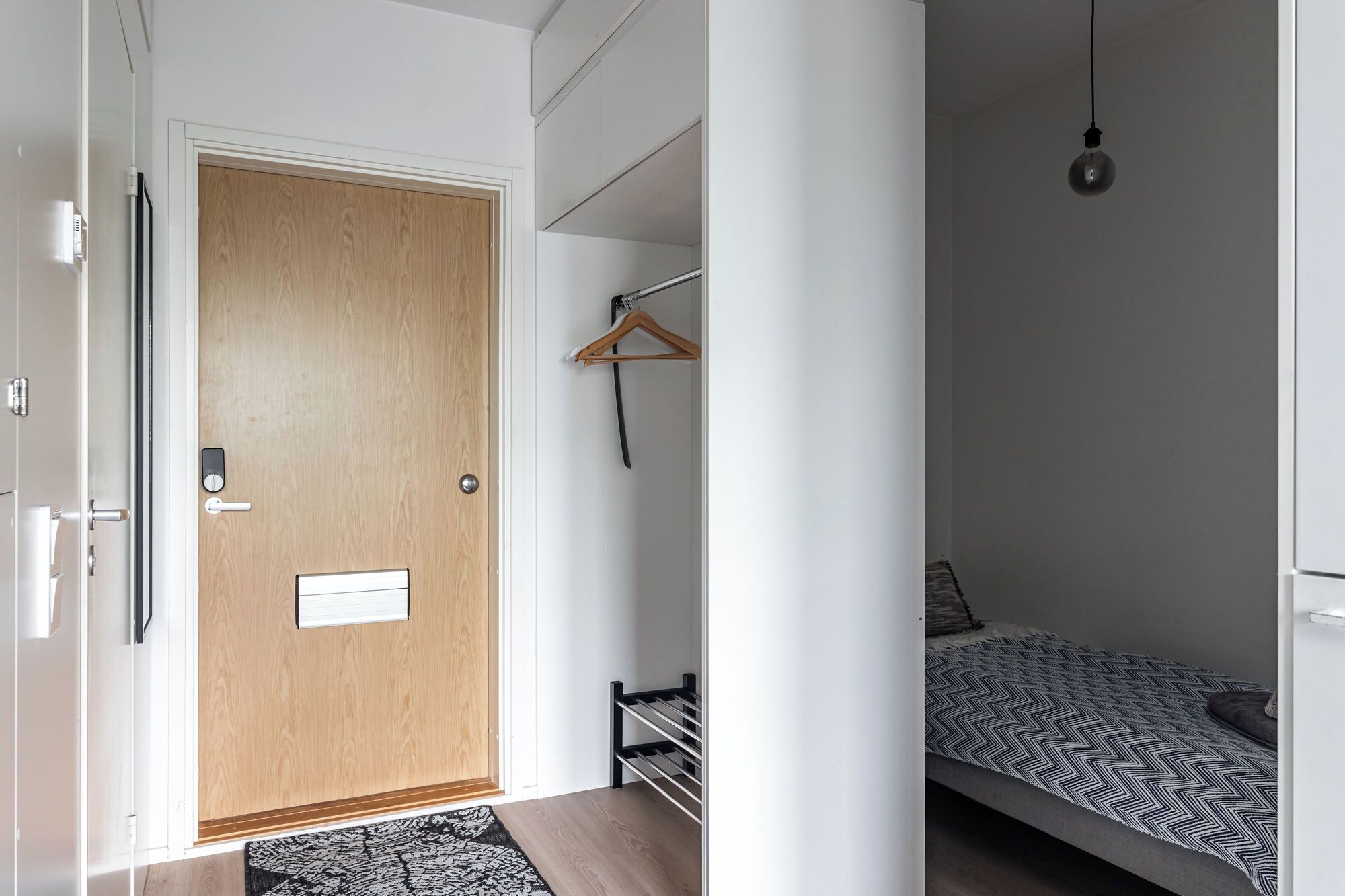 A bedroom with a bed, a hanging light, and a door with a wooden panel.