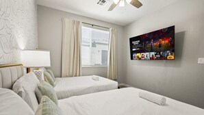 Camera d'albergo con due letti, una ventola a soffitto, una finestra con tende e un televisore a parete che mostra un manifesto cinematografico.