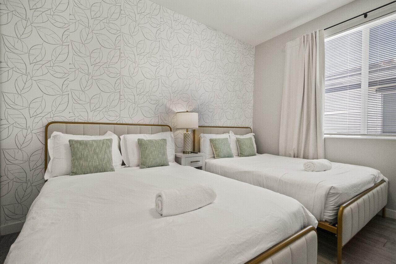 Une chambre d’hôtel avec deux lits, une table de chevet, une lampe et une fenêtre avec des stores.