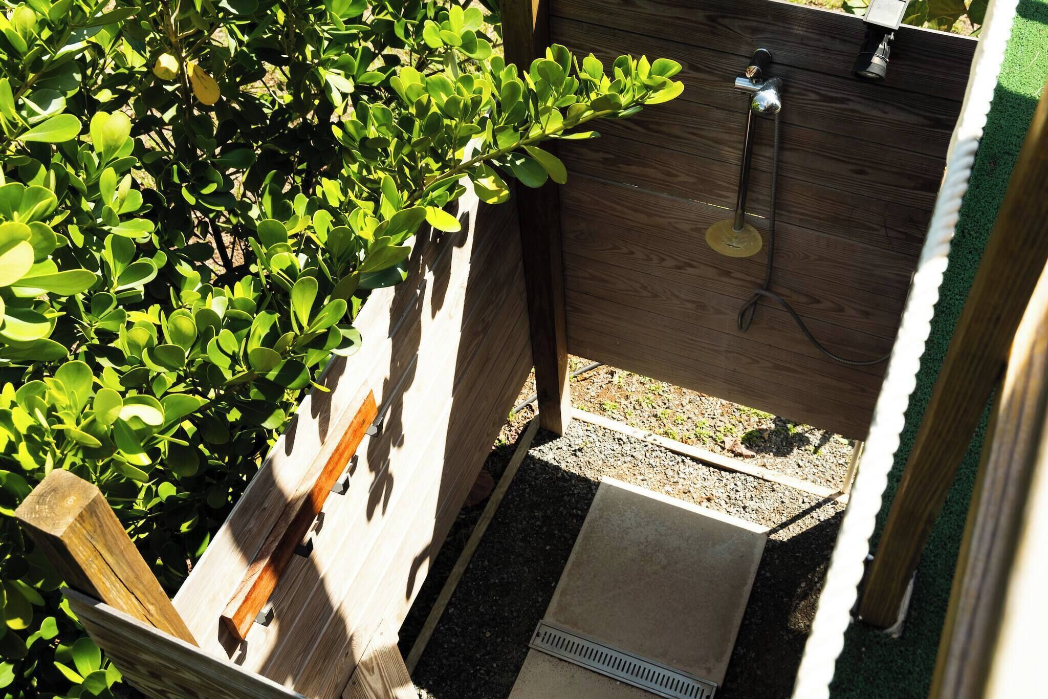 A small, enclosed outdoor shower area with a wooden wall and a metal hose.