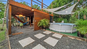 A wooden structure with a hammock, a hot tub, and a small pool.