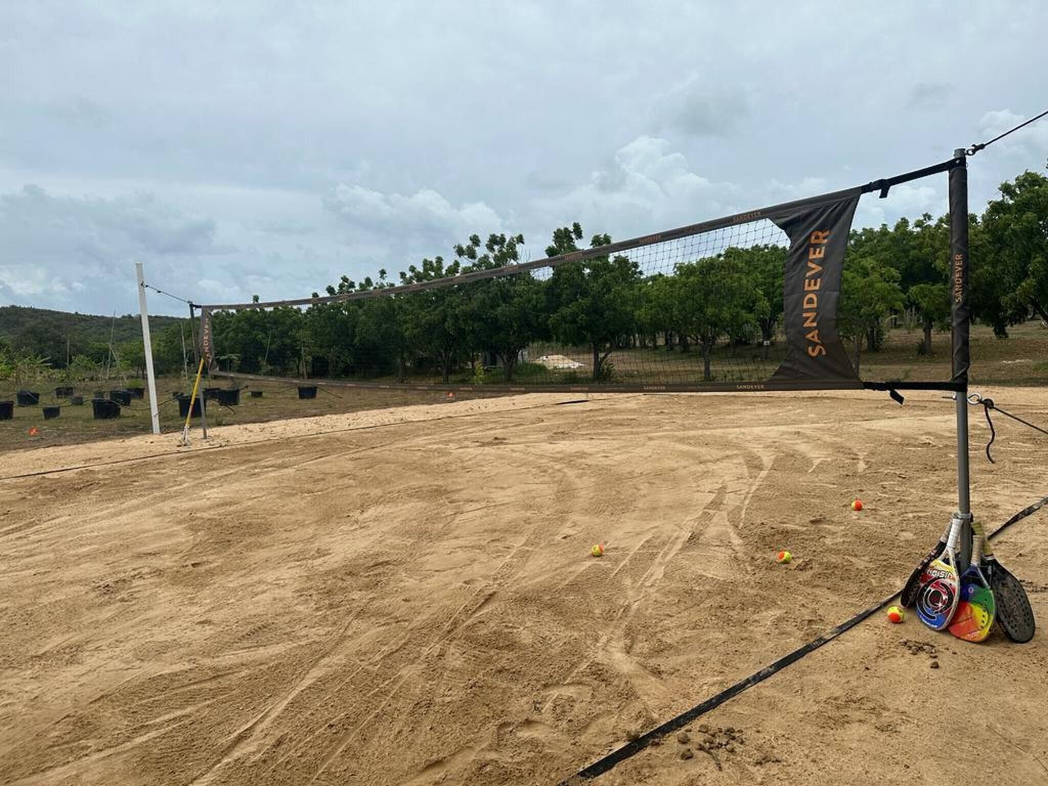 An outdoor tennis court with a net, surrounded by trees and a cloudy sky.