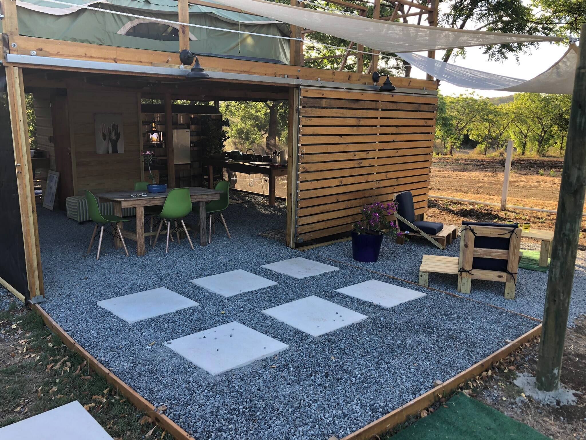 A wooden outdoor seating area with a table and chairs, surrounded by gravel and stepping stones.
