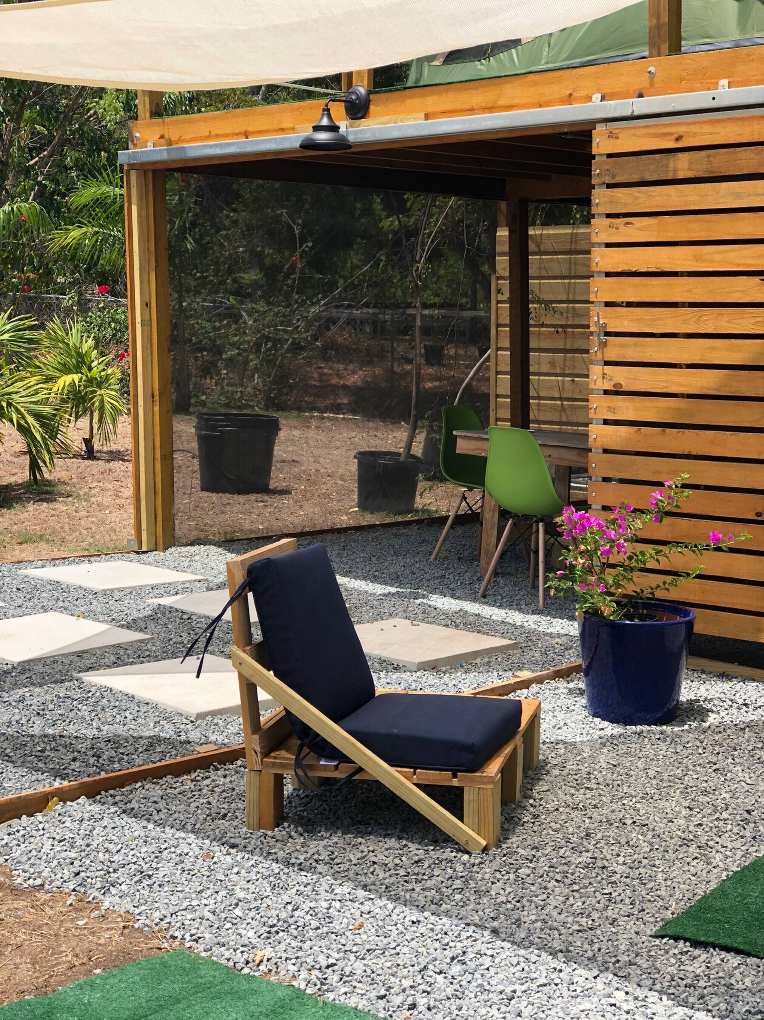 A wooden deck with a chair and a potted plant, surrounded by gravel and greenery.